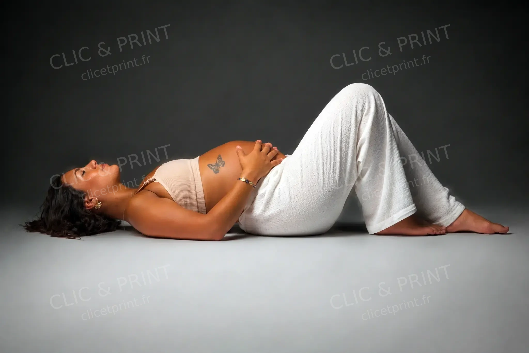 Femme enceinte allongée dans une tenue blanche lors d’une séance au studio
