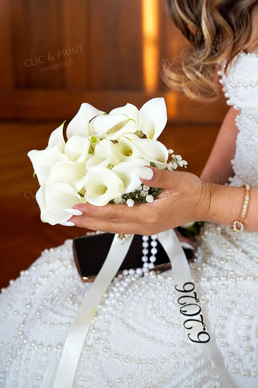 Bouquet d’arums blancs dans les mains de la mariée, robe perlée et ruban