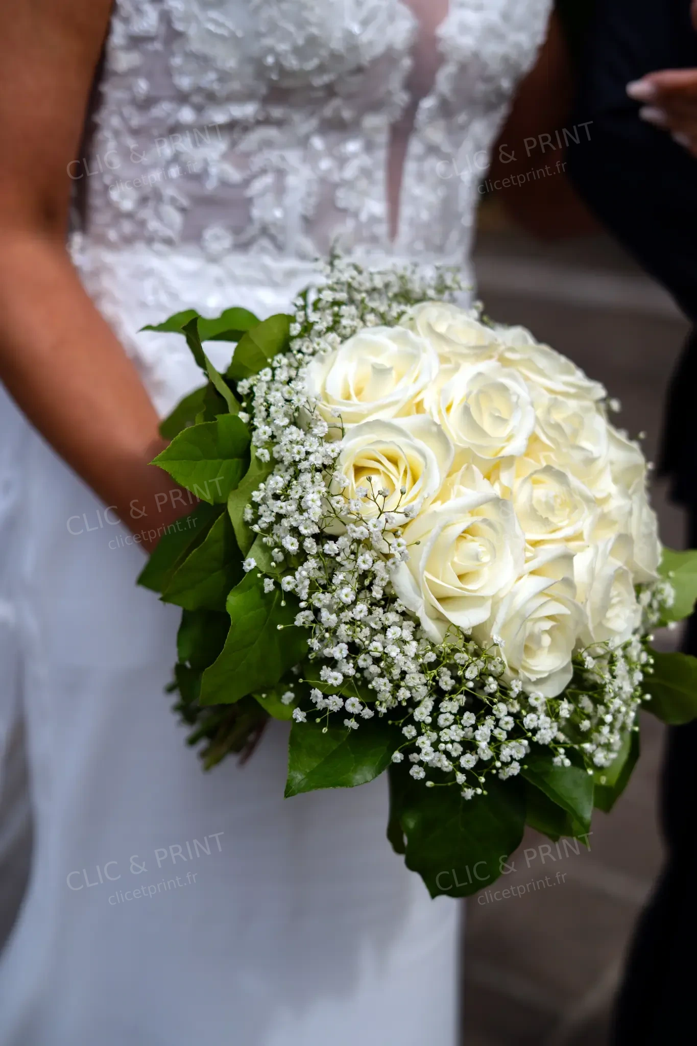 Bouquet de roses blanches et feuillage devant la robe de mariée